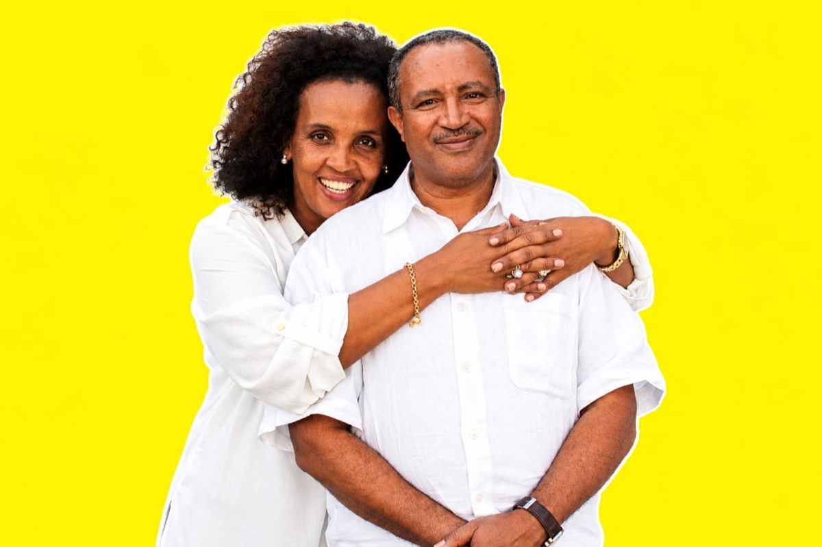 Dr. Worku Mekonnen Bogale smiling with his wife's arms around him, in white shirts against a yellow background